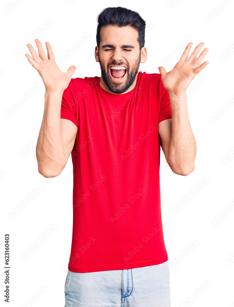 Fototapeta premium Young handsome man with beard wearing casual t-shirt celebrating mad and crazy for success with arms raised and closed eyes screaming excited. winner concept