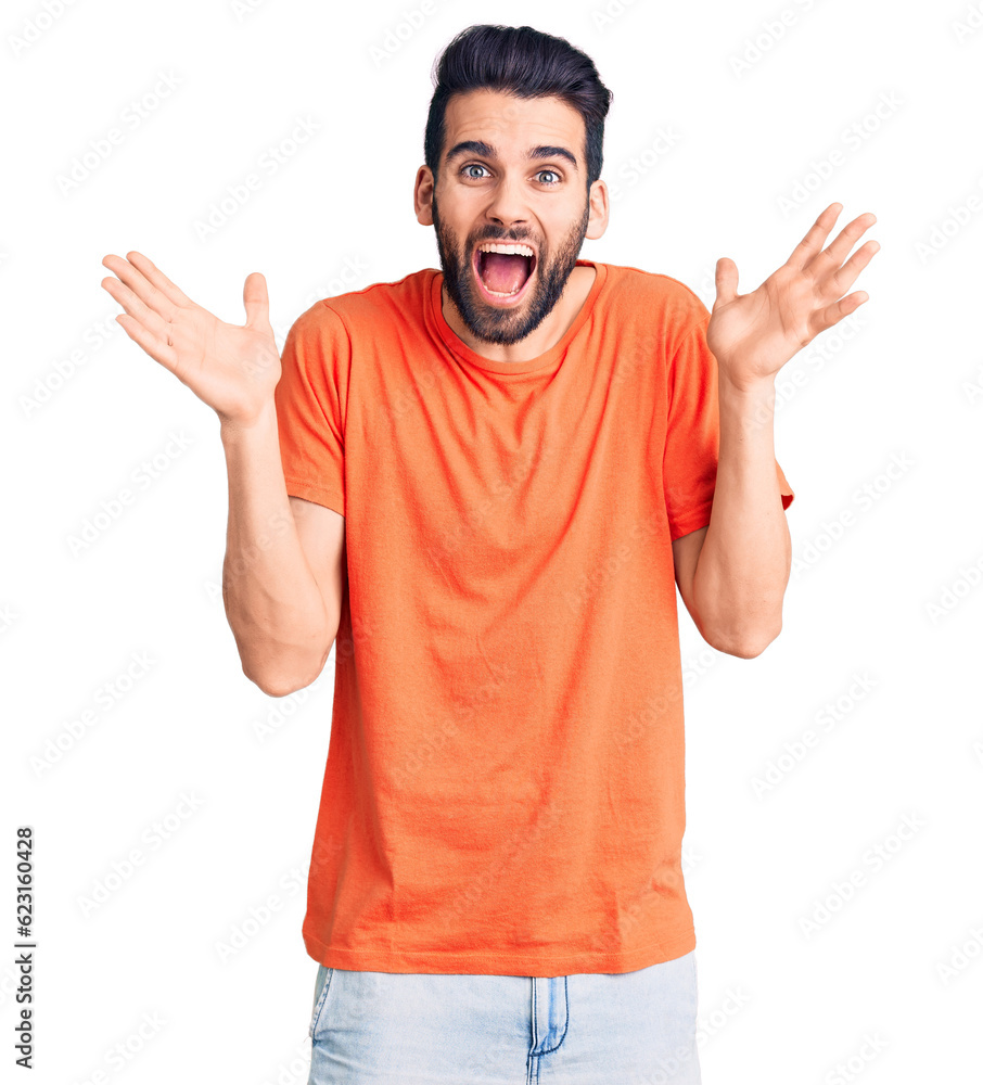 Young handsome man with beard wearing casual t-shirt celebrating crazy and amazed for success with arms raised and open eyes screaming excited. winner concept Young handsome man with beard wearing casual t-shirt celebrating crazy and amazed for success with arms raised and open eyes screaming excited. winner concept