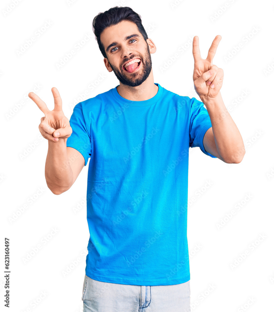 Young handsome man with beard wearing casual t-shirt smiling with tongue out showing fingers of both hands doing victory sign. number two. Young handsome man with beard wearing casual t-shirt smiling with tongue out showing fingers of both hands doing victory sign. number two.