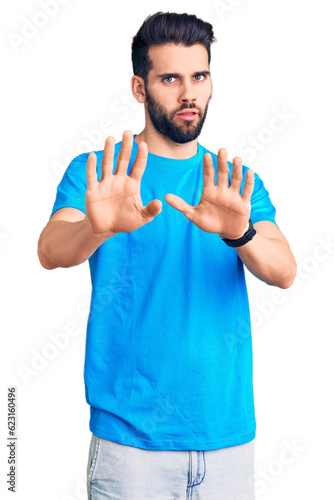 Young handsome man with beard wearing casual t-shirt moving away hands palms showing refusal and denial with afraid and disgusting expression. stop and forbidden.