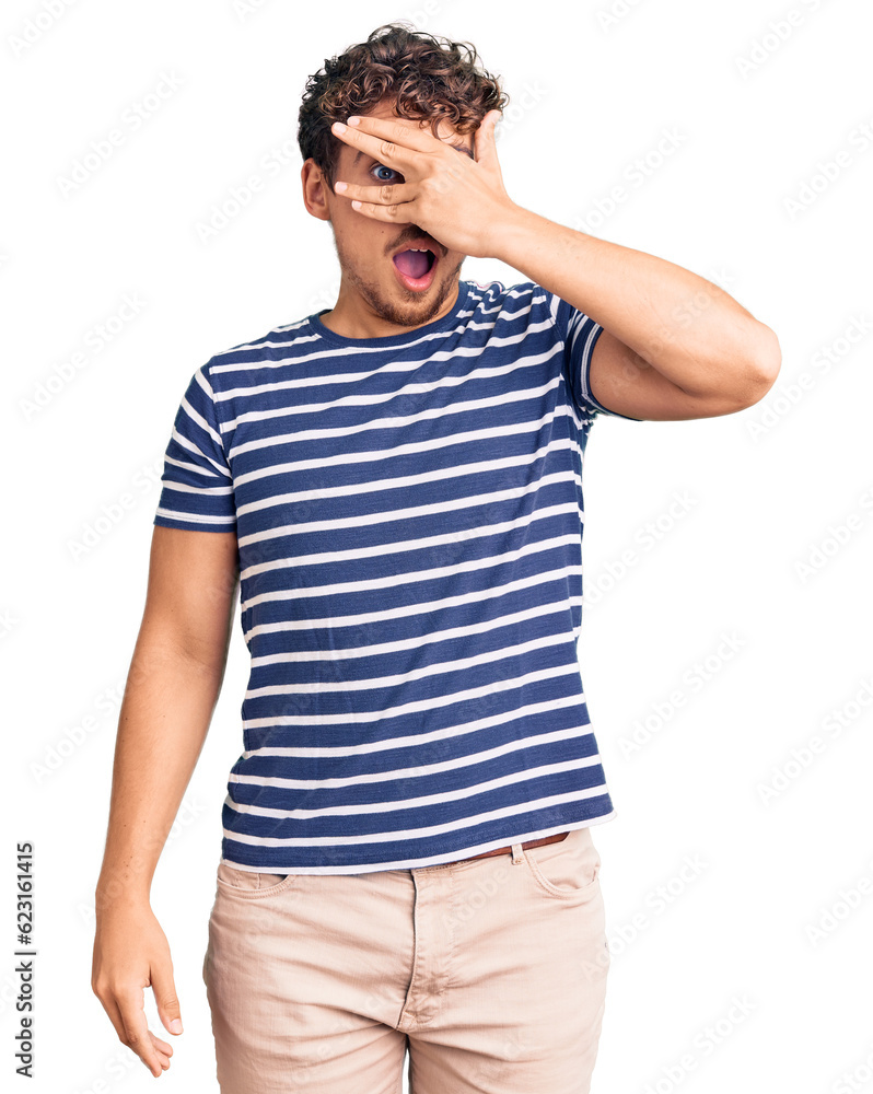 Young handsome man with curly hair wearing casual clothes peeking in shock covering face and eyes with hand, looking through fingers with embarrassed expression. Young handsome man with curly hair wearing casual clothes peeking in shock covering face and eyes with hand, looking through fingers with embarrassed expression.