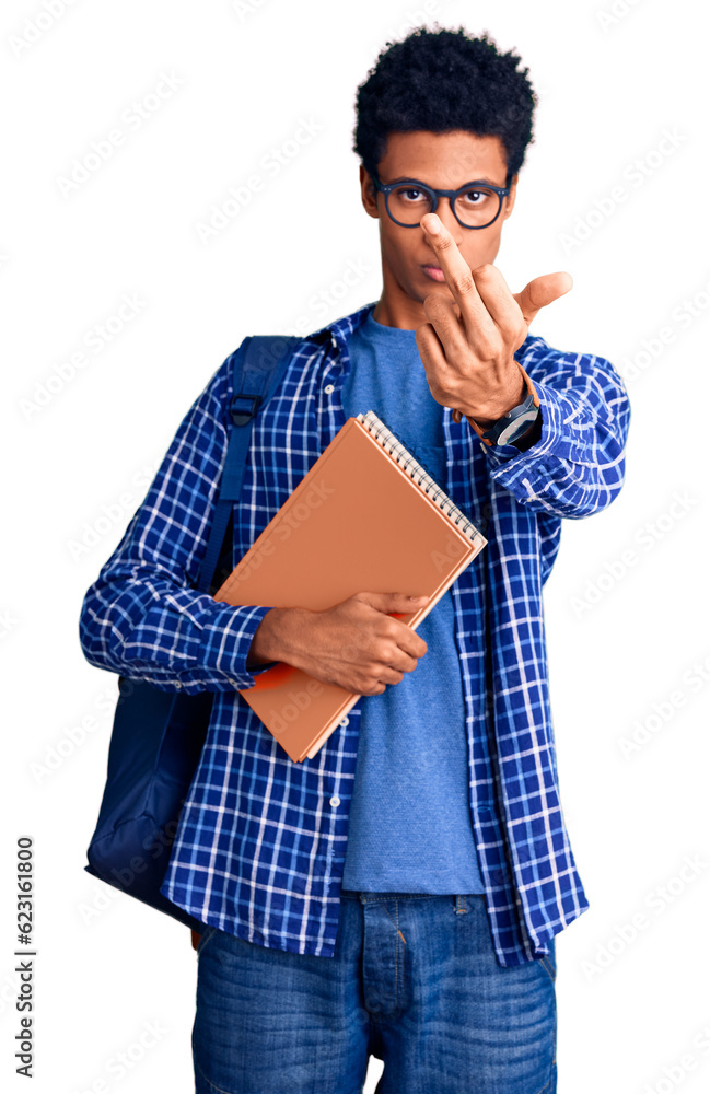 Young african american man wearing student backpack holding book showing middle finger, impolite and rude fuck off expression Young african american man wearing student backpack holding book showing middle finger, impolite and rude fuck off expression