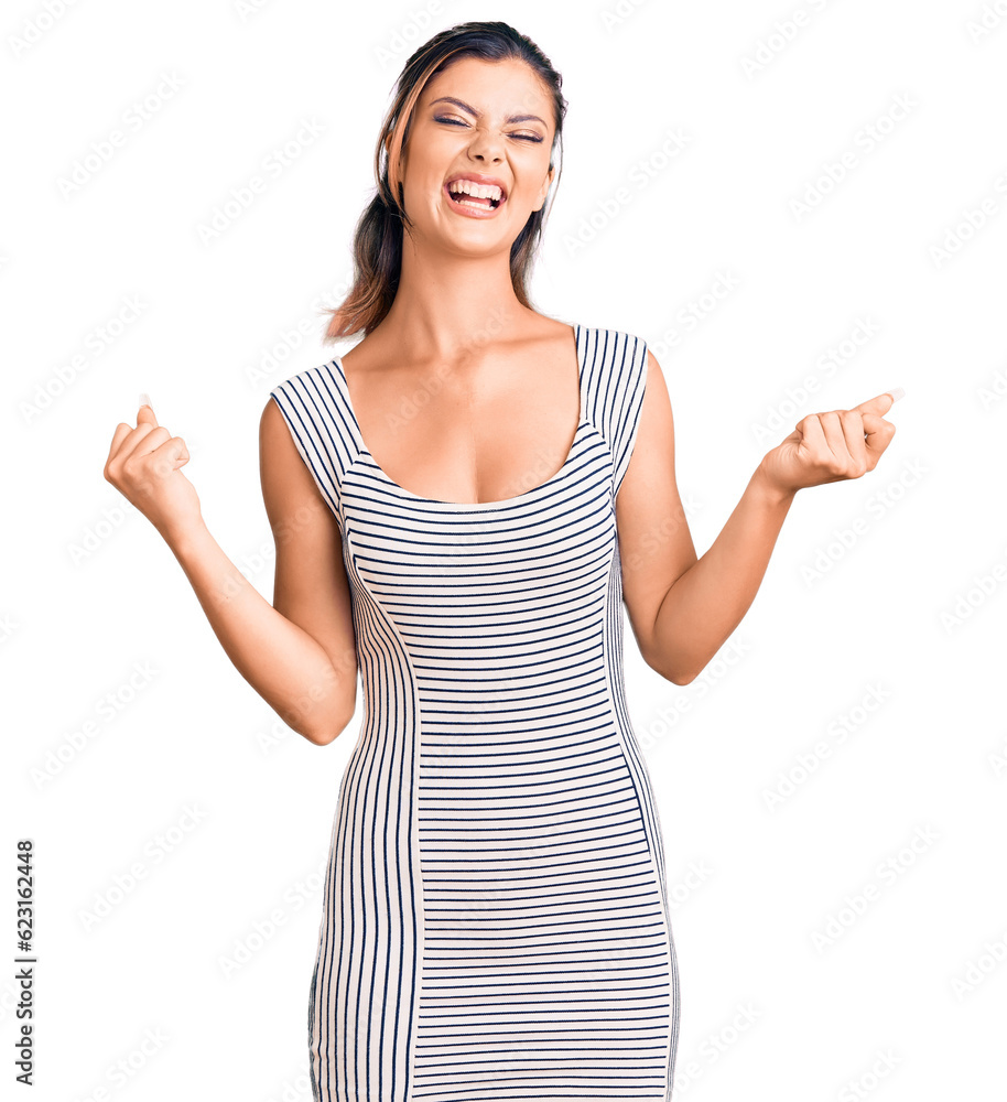 Young beautiful woman wearing casual dress very happy and excited doing winner gesture with arms raised, smiling and screaming for success. celebration concept. Young beautiful woman wearing casual dress very happy and excited doing winner gesture with arms raised, smiling and screaming for success. celebration concept.