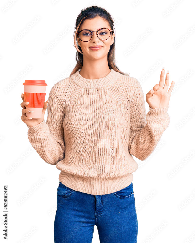 Young beautiful woman wearing glasses holding takeaway cup of coffee doing ok sign with fingers, smiling friendly gesturing excellent symbol Young beautiful woman wearing glasses holding takeaway cup of coffee doing ok sign with fingers, smiling friendly gesturing excellent symbol