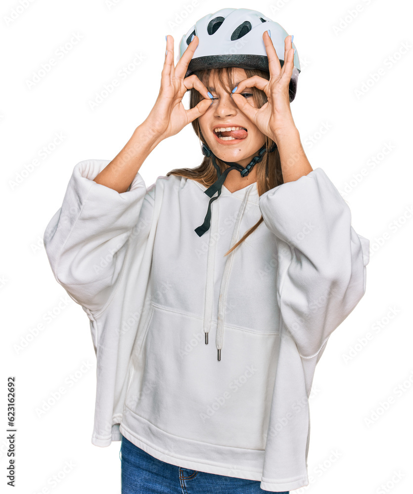 Teenager caucasian girl wearing bike helmet doing ok gesture like binoculars sticking tongue out, eyes looking through fingers. crazy expression. Teenager caucasian girl wearing bike helmet doing ok gesture like binoculars sticking tongue out, eyes looking through fingers. crazy expression.