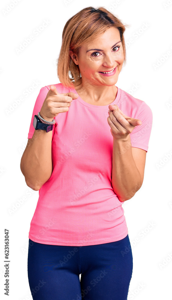 Young blonde woman wearing sportswear pointing fingers to camera with happy and funny face. good energy and vibes. Young blonde woman wearing sportswear pointing fingers to camera with happy and funny face. good energy and vibes.