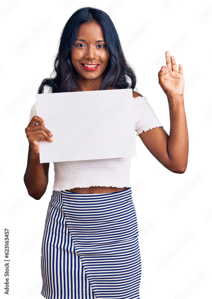 Young indian girl holding blank empty banner doing ok sign with fingers, smiling friendly gesturing excellent symbol Young indian girl holding blank empty banner doing ok sign with fingers, smiling friendly gesturing excellent symbol