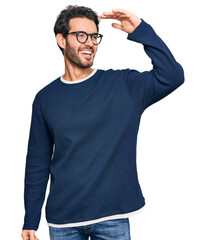 Young hispanic man wearing casual clothes and glasses very happy and smiling looking far away with hand over head. searching concept.