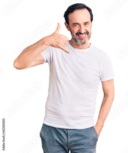 Middle age handsome man wearing casual t-shirt smiling doing phone gesture with hand and fingers like talking on the telephone. communicating concepts.