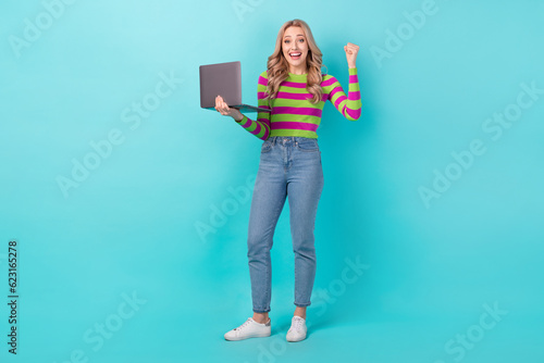 Full length photo of shiny lucky woman dressed striped sweater winning game modern gadget isolated turquoise color background