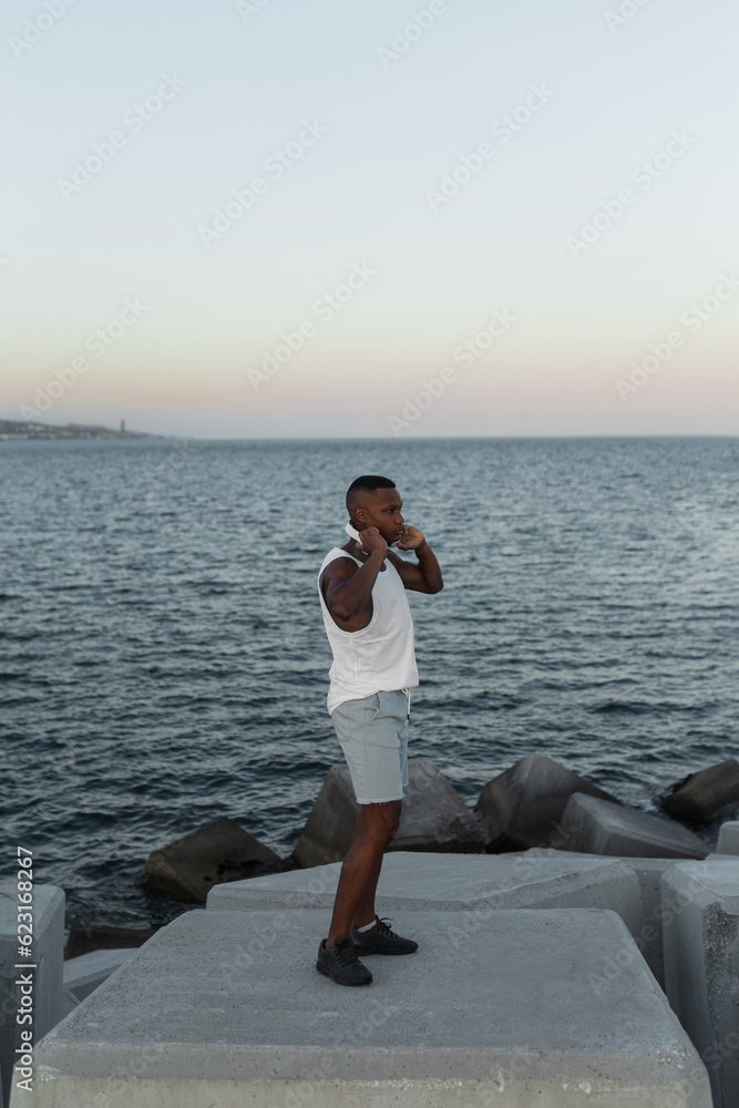 Slim black male stretching on seafront during training Slim black male stretching on seafront during training