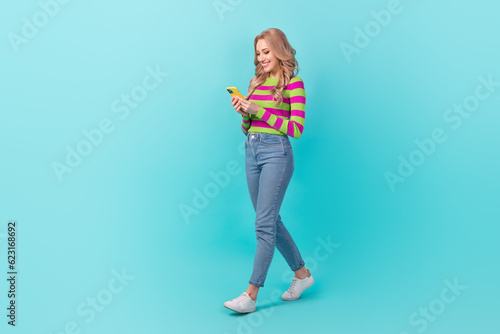Full length photo of shiny adorable lady wear striped pullover walking communicating modern device isolated teal color background