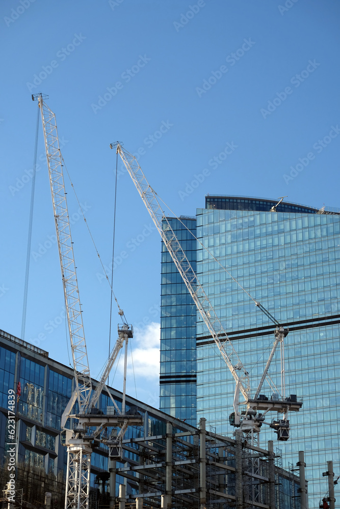 Yellow hoisting tower cranes in construction process of constructing skyscraper over blue sky