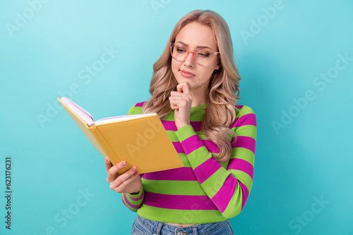 Photo of intelligent minded woman dressed striped sweatshirt look at interesting book hand on chin isolated on teal color background