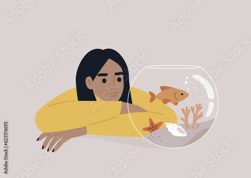 A young Caucasian person watching a goldfish swimming in a round water tank