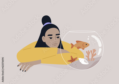 A young Asian person watching a goldfish swimming in a round water tank