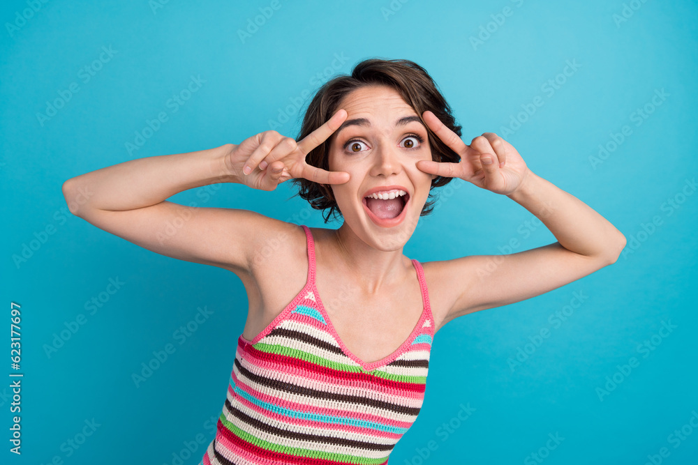 Photo of funky adorable woman dressed tank top showing two v-signs cover eyes isolated blue color background Photo of funky adorable woman dressed tank top showing two v-signs cover eyes isolated blue color background