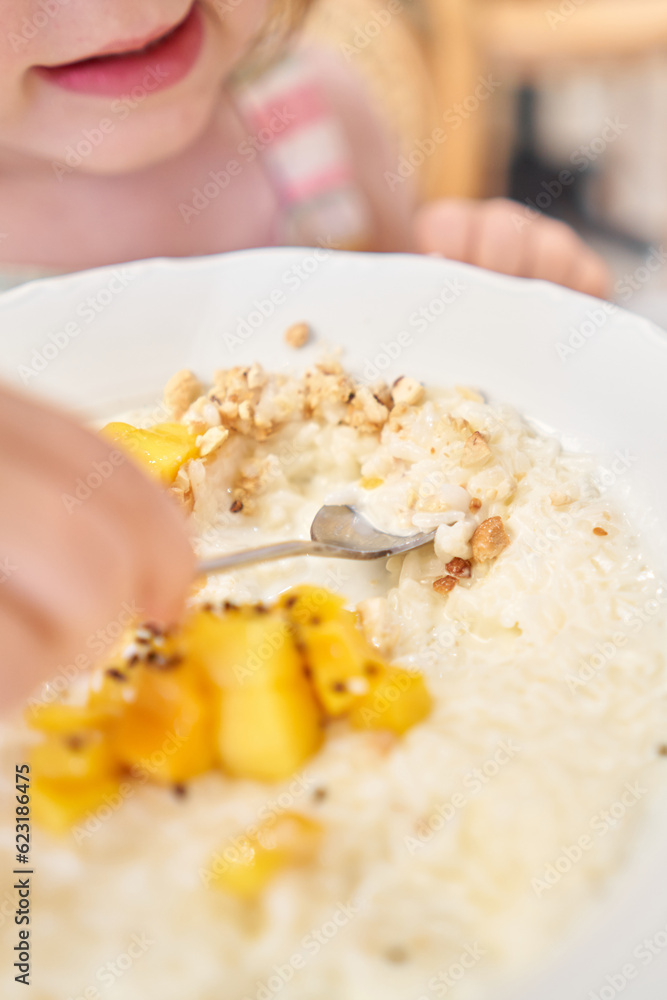 Little kid having breakfast at cafe. Adorable girl drinking still water, eating rice porridge with mango. enjoying breakfast. Little kid having breakfast at cafe. Adorable girl drinking still water, eating rice porridge with mango. enjoying breakfast.