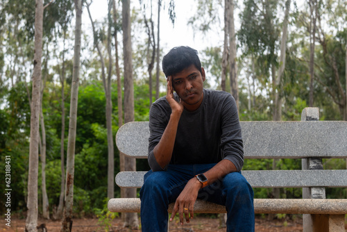 A portrait of a depressed Indian man sitting on a bench in a park.