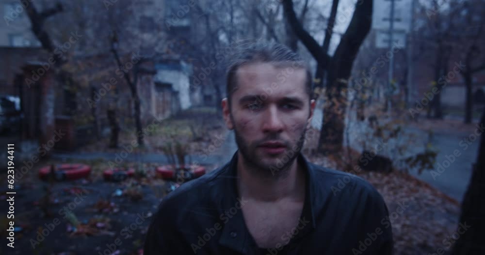 Exhausted, frozen young man in leather jacket walks down the street in ghetto during the first snow. Dark moody scene of a sullen, bad-looking man with an emotion of indifference on his face. Exhausted, frozen young man in leather jacket walks down the street in ghetto during the first snow. Dark moody scene of a sullen, bad-looking man with an emotion of indifference on his face.