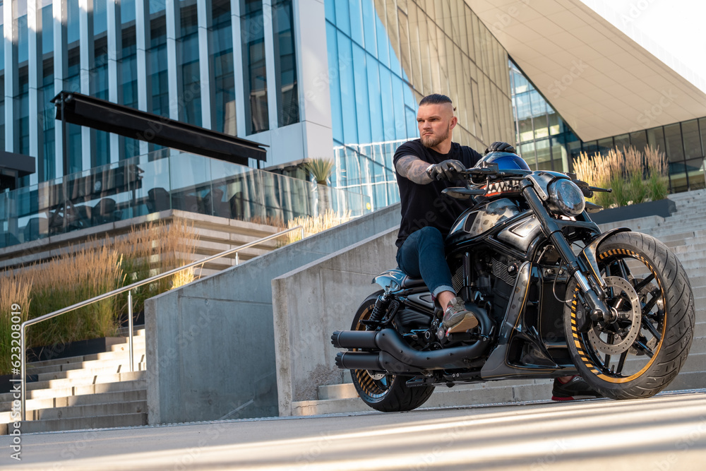 Handsome biker without helmet sitting on his moto against urban background Handsome biker without helmet sitting on his moto against urban background