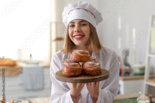 Female baker with board of tasty buns in kitchen, closeup