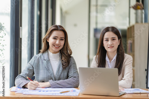 Two asian businesswoman sitting and consulting business inside modern office discussing presentation of startup project idea Analyze statistics and investment markets at the office.