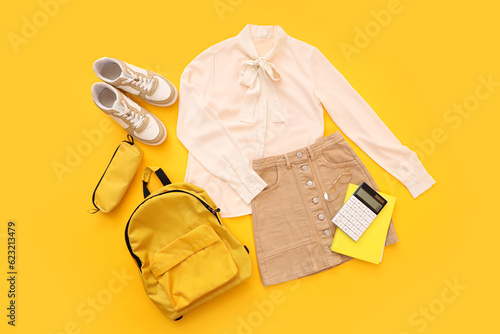 Composition with stylish school uniform, backpack, sneakers and stationery on orange background