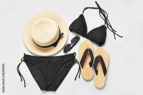 Stylish swimsuit, hat, sunglasses and flip-flops on light background