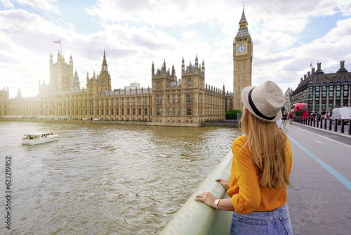 Tourism in London. Back view of traveler girl enjoying sight of Westminster palace and bridge on Thames with famous Big Ben tower in London, UK. photo