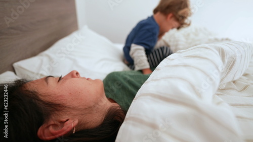 Child getting up from bed in morning rubbing eye next to mother kid wakes up