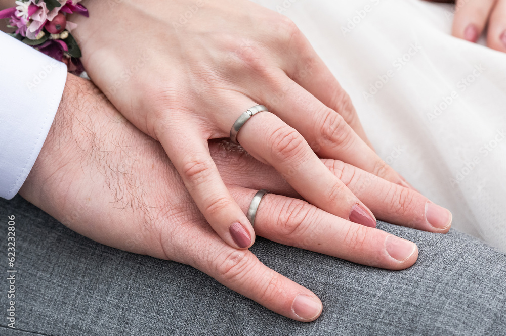 Bride holding groom hand with wedding rings sitting on bench Bride holding groom hand with wedding rings sitting on bench