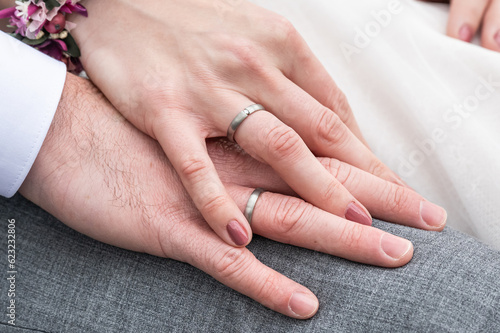 Bride holding groom hand with wedding rings sitting on bench
