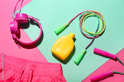 Bottle of sunscreen cream, skipping ropes, headphones and clothes on color background