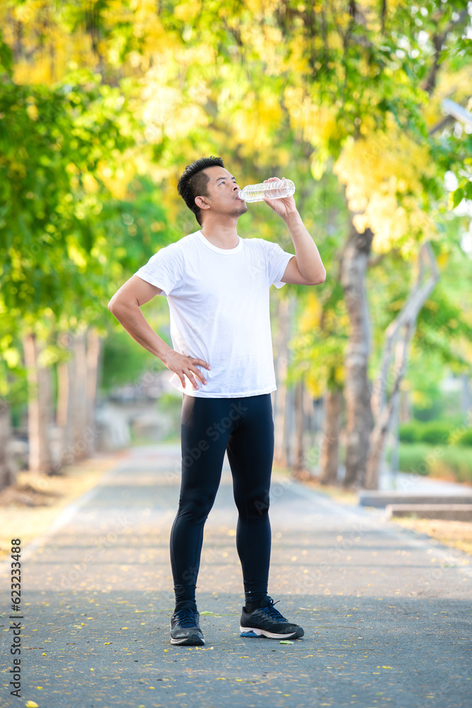 A man with whiteshirt on drinking water on running way with tree bloom background A man with whiteshirt on drinking water on running way with tree bloom background