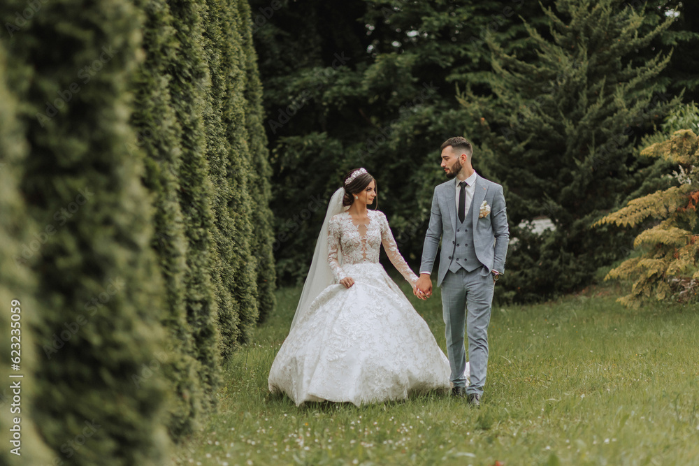 European wedding couple walking in the park. The bride in a beautiful dress with sleeves and a crown on her head. Groom with a black beard of Caucasian appearance in a classic suit.