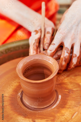 Teaching a child to make pottery from red clay. Clay pottery hands close up working on wheel handcrafts. Clay crockery making. Working with red clay. Hands and fingers of potter and child in clay.