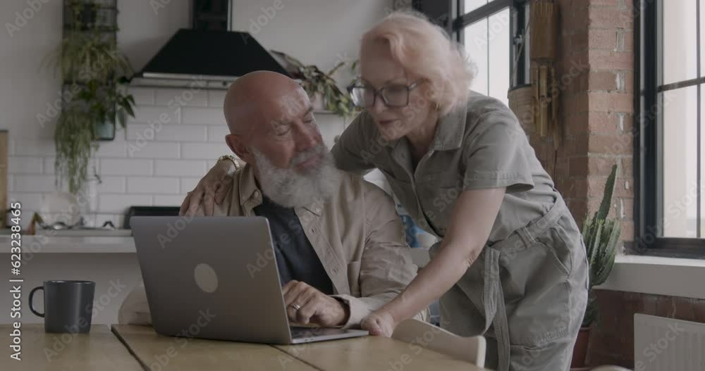 Senior Adult Couple using Laptop at Home in Kitchen Senior Adult Couple using Laptop at Home in Kitchen