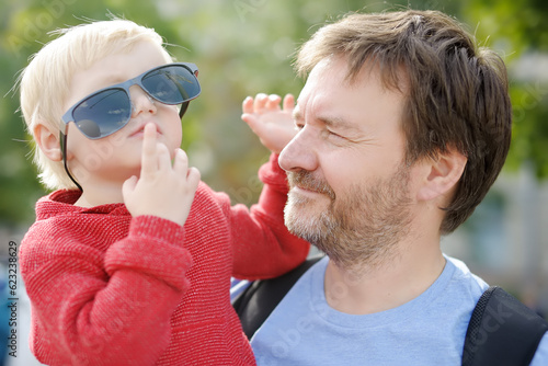 Mature father holds a child in his arms. Funny little boy trying on dad's sunglasses.