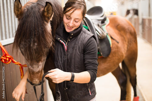 How to use horse bridle muzzle. Mid adult woman prepare in horse riding school for training