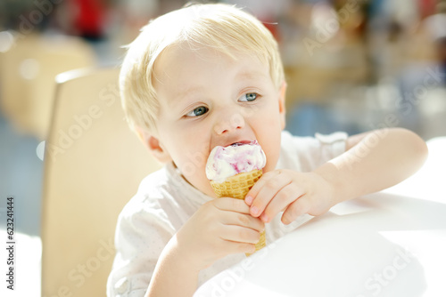 Cute little boy eating ice cream in a waffle cone. Child is tasting gelato in Italian cafe. Unhealthy street fast food.
