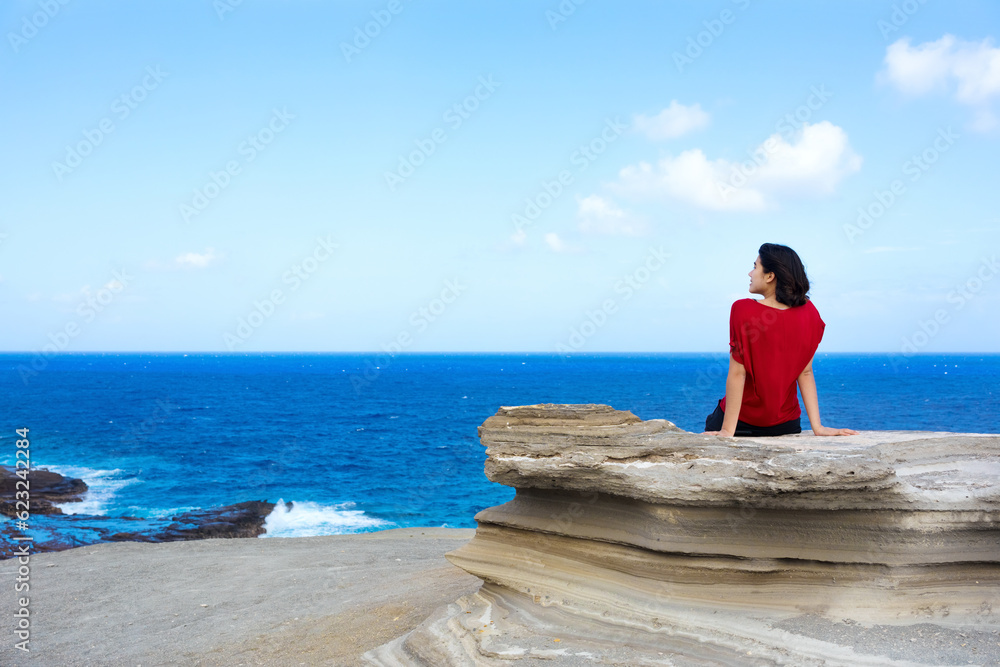 Young woman sitting on large rock cliff  by Hawaiian  ocean