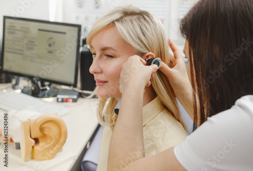 Woman patient having check-up of hearing at doctor otolaryngologist. Hearing exam for female. Otolaryngologist doctor checking mature woman's ear using otoscope or auriscope at medical clinic
