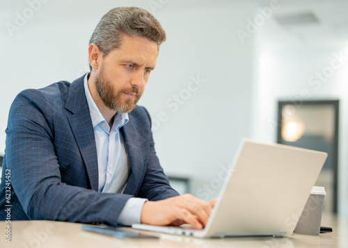 Man with laptop at office. Business man in suit in office work on laptop computer. Office worker using laptop. Business man work on laptop. Businessman have online work in modern office interior.