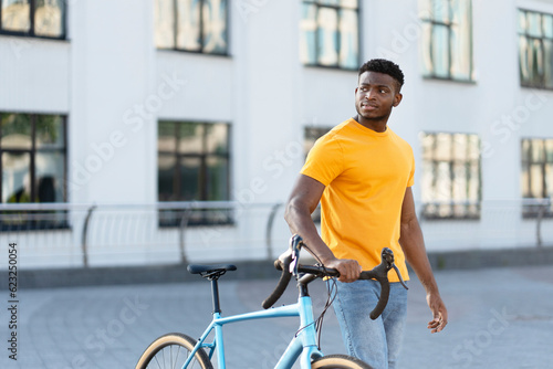 Dark skinned handsome man walking street near bicycle while looking away © Maria Vitkovska