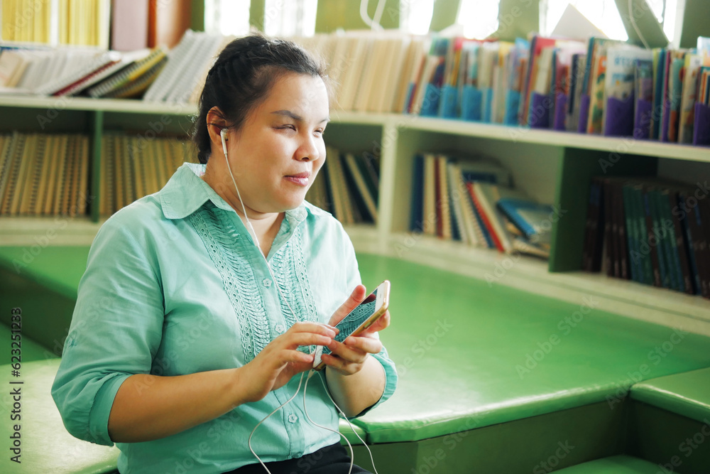 Portrait of Asian woman with blindness disability wearing earphones using smart phone with voice accessibility for persons with visual impairment disabilities in creative workplace library. - obrazy, fototapety, plakaty 