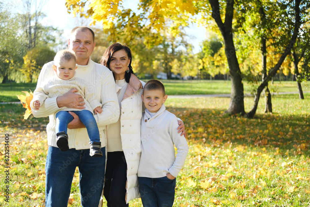 Fototapeta premium A happy family of four spend time in the autumn park. Family smiling and looking at the camera