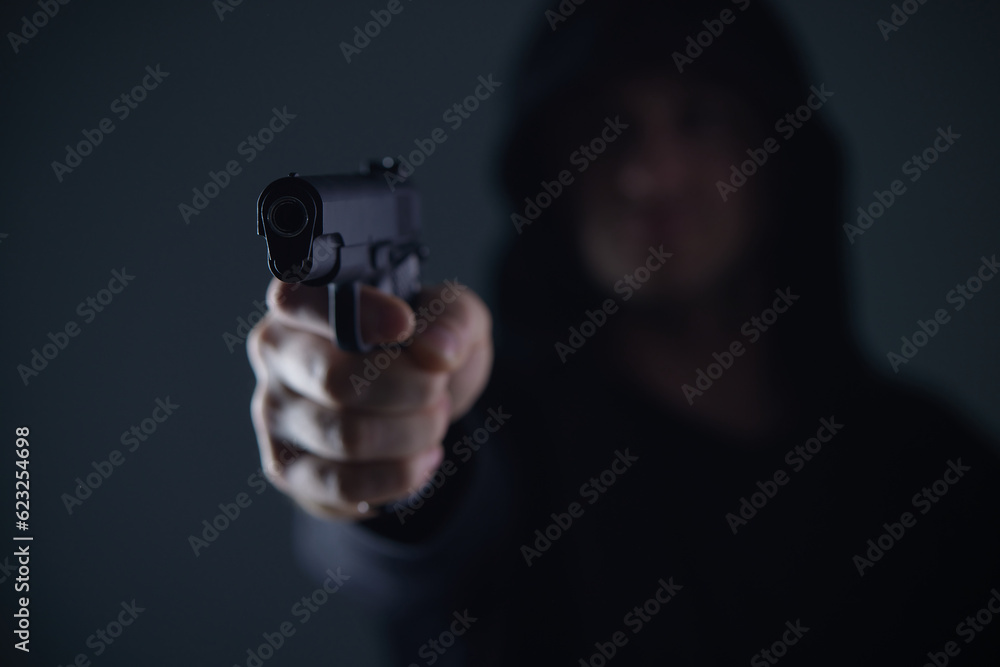 robber with gun aiming into camera. Man in hood threatens with firearm. Weapon in person's hands. Murderer or armed thief. Criminal with pistol. robber with gun aiming into camera. Man in hood threatens with firearm. Weapon in person's hands. Murderer or armed thief. Criminal with pistol.