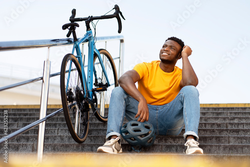 Dreamy happy african american man looking away while relaxing at the stairs