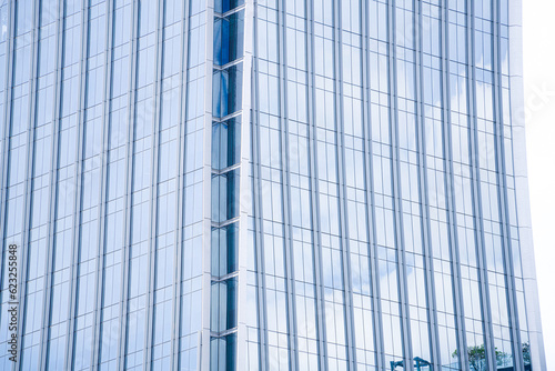 Perspective and underside angle view to textured background of contemporary glass facade of achitecture building skyscrapers with light reflect of sky and cloud. (Detail curve shape of glass mullion) photo